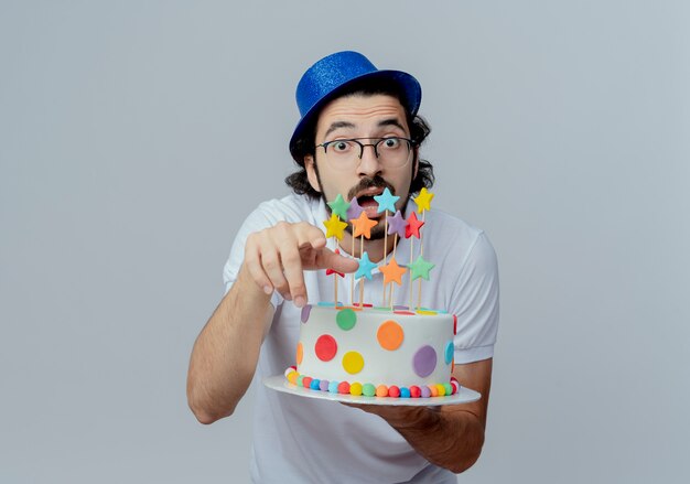 Hombre guapo sorprendido con gafas y sombrero azul sosteniendo pastel y mostrando gesto aislado en blanco