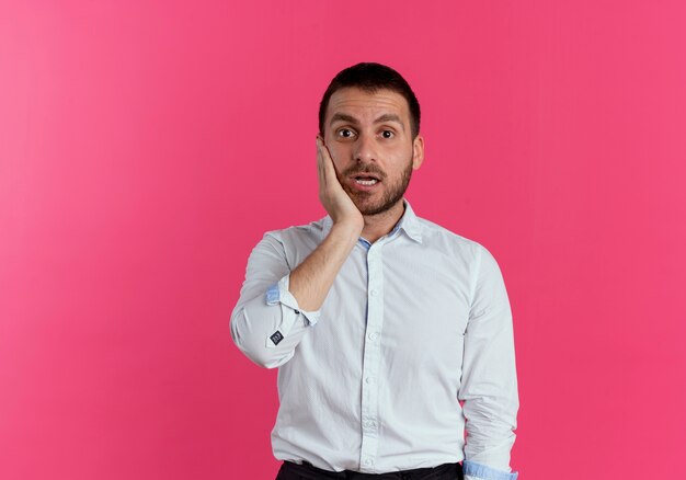 Hombre guapo sorprendido pone la mano en la cara mirando aislado en la pared rosa