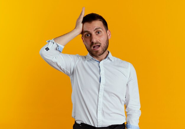 Hombre guapo sorprendido pone la mano en la frente aislada en la pared naranja