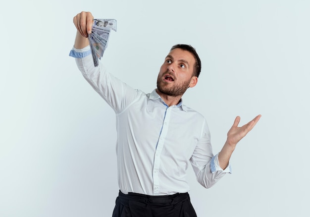 Foto gratuita hombre guapo sorprendido sostiene y mira dinero aislado en la pared blanca