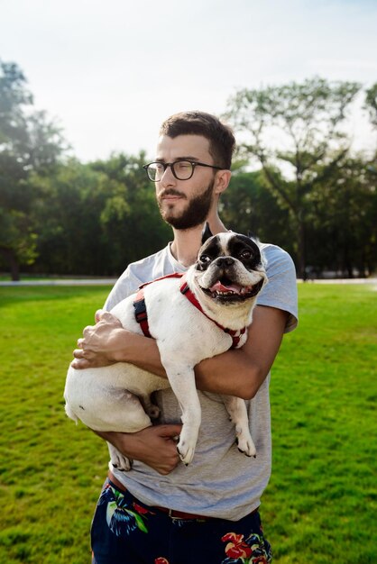 Hombre guapo sosteniendo bulldog francés caminando en el parque