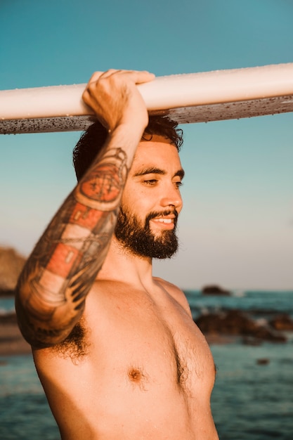 Foto gratuita hombre guapo con tabla de surf en la cabeza