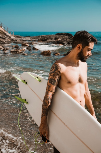 Hombre guapo con tabla de surf cerca del mar limpio