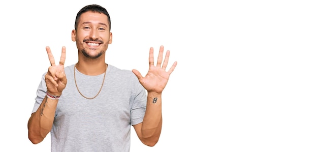Foto gratuita hombre guapo con tatuajes con estilo de los años 90 mostrando y señalando con los dedos número siete mientras sonríe confiado y feliz.