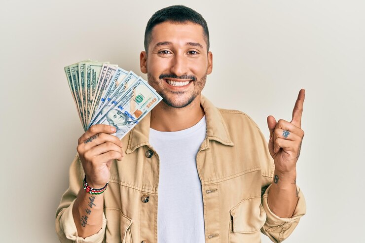 Foto gratuito hombre guapo con tatuajes sosteniendo dólares sonriendo feliz señalando con la mano y el dedo al lado