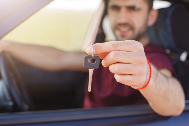 Hombre guapo tiene la llave del coche mientras se sienta en automóvil