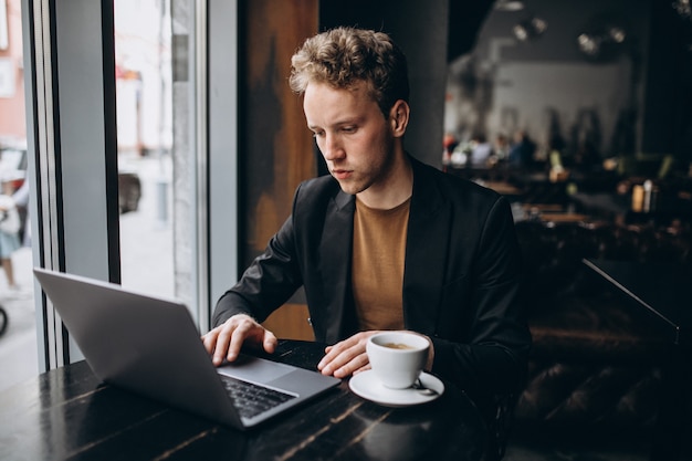 Hombre guapo trabajando en una computadora en un café y tomando café