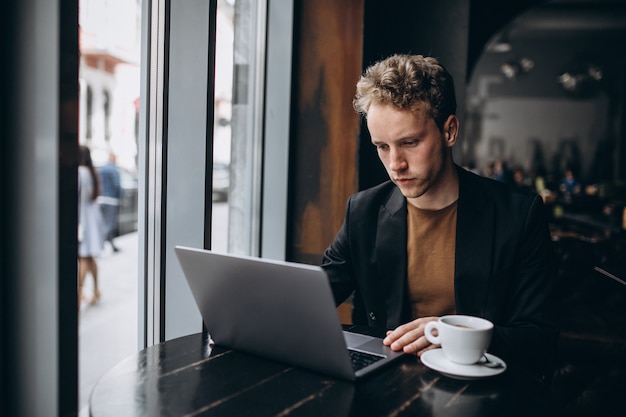 Hombre guapo trabajando en una computadora en un café y tomando café