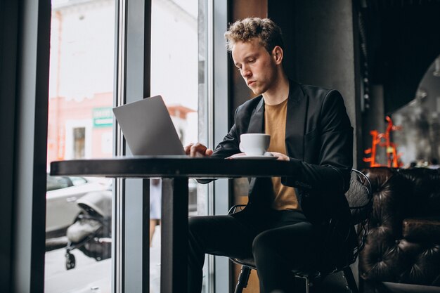 Hombre guapo trabajando en una computadora en un café y tomando café