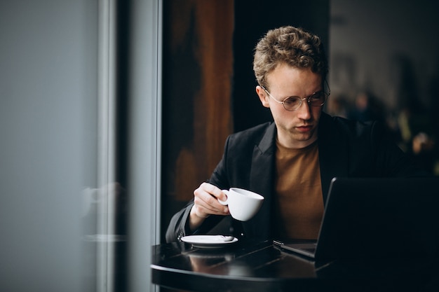 Hombre guapo trabajando en una computadora en un café y tomando café