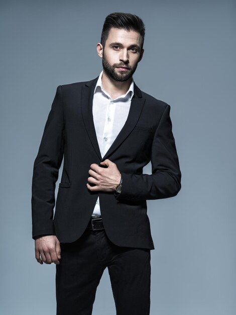 Hombre guapo en traje negro con camisa blanca - posando Chico atractivo con peinado de moda. Hombre confiado con barba corta. Chico adulto con cabello castaño. Retrato completo.