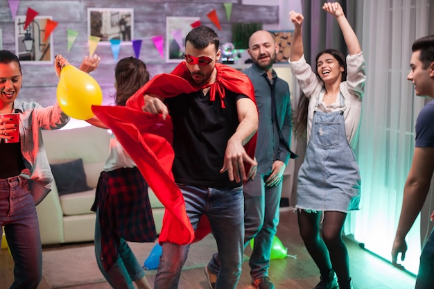 Hombre guapo en traje de superhéroe bailando con música disco en la fiesta de amigos.