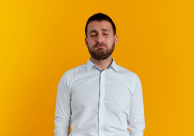 Hombre guapo triste se encuentra con los ojos cerrados aislados en la pared naranja