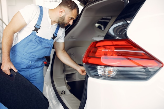 Foto gratuita hombre guapo en uniforme azul comprueba el coche