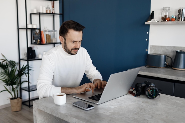 Foto gratuito hombre guapo usando una laptop en casa en la cocina