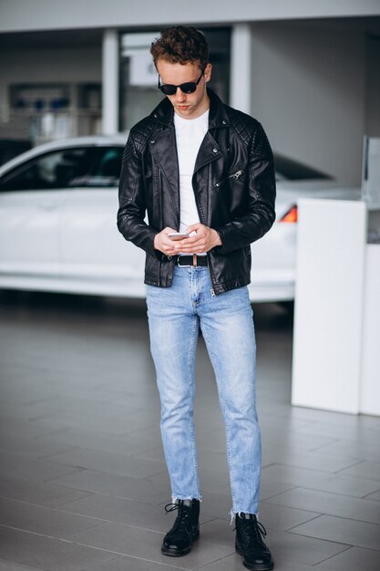 Hombre guapo usando el teléfono en una sala de exposición de coches