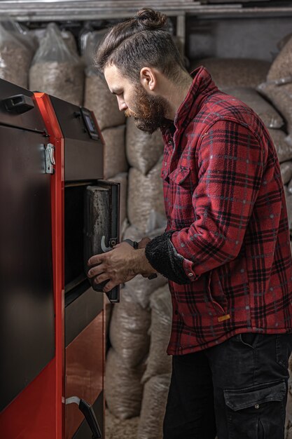 Un hombre en una habitación con una caldera de combustible sólido, trabajando en biocombustible, calefacción económica.