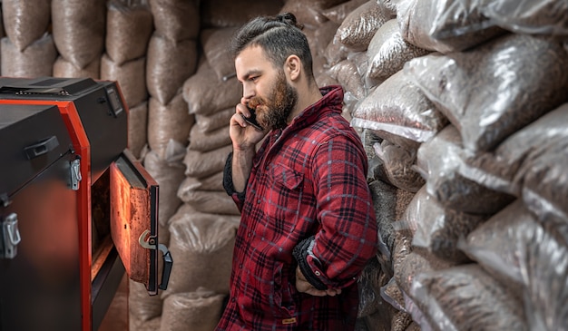 Un hombre en una habitación con una caldera de combustible sólido, trabajando en biocombustible, calefacción económica.