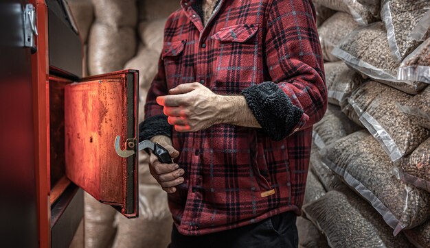 Un hombre en una habitación con una caldera de combustible sólido, trabajando en biocombustible, calefacción económica.