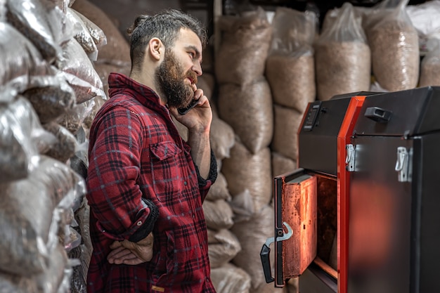 Un hombre en una habitación con una caldera de combustible sólido, trabajando en biocombustible, calefacción económica.