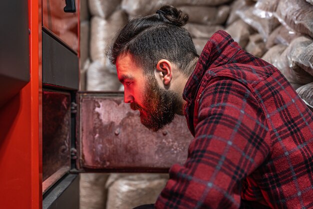 Un hombre en una habitación con una caldera de combustible sólido, trabajando en biocombustible, calefacción económica.