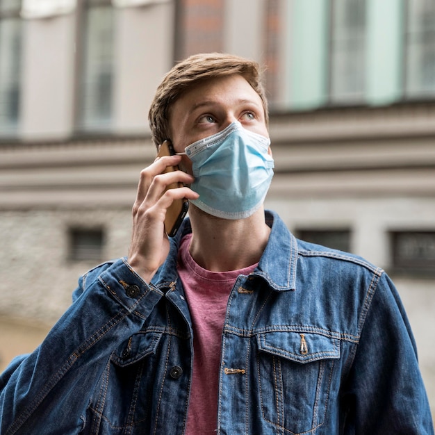 Hombre hablando por su teléfono mientras usa una máscara médica afuera