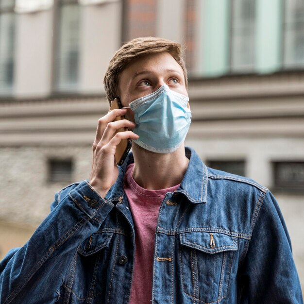 Hombre hablando por su teléfono mientras usa una máscara médica afuera