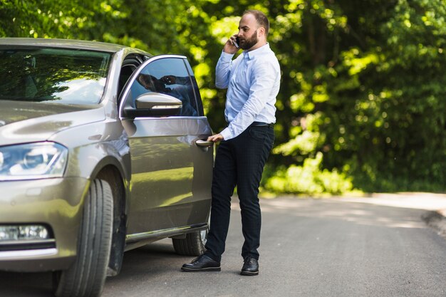Hombre hablando por teléfono inteligente abriendo la puerta del coche