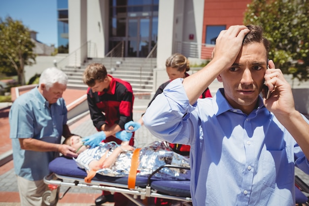 Foto gratuita hombre hablando por teléfono móvil y paramédicos examinando niño herido en segundo plano.