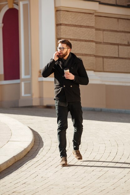 Hombre hablando por teléfono móvil y tomando café en la ciudad