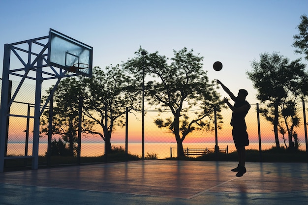 Foto gratuita hombre haciendo deporte, jugando baloncesto al amanecer, saltando silueta