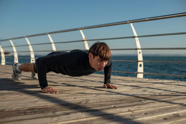 Hombre haciendo flexiones en ropa deportiva en la playa