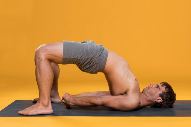 Hombre haciendo puente pose en estera de yoga