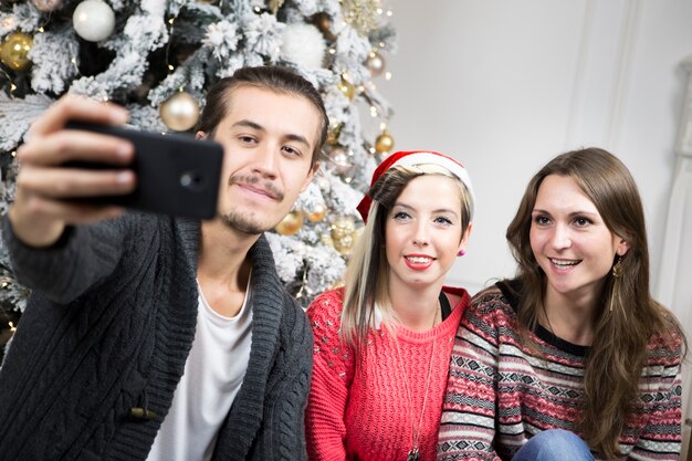 Hombre haciendo selfie con amigos enfrente de árbol de navidad
