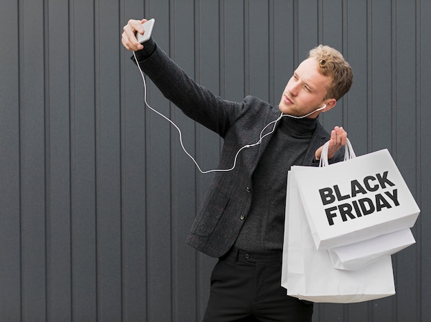 Hombre haciendo un selfie mientras sostiene bolsas de compras de viernes negro