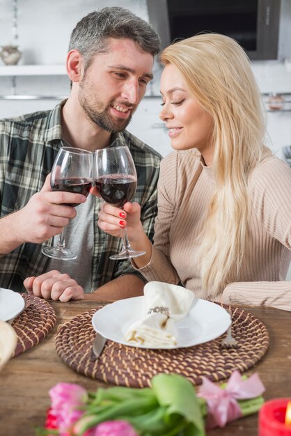 Hombre haciendo sonar vasos con mujer en mesa con flores y platos