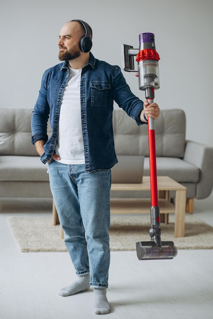 Foto gratuita hombre haciendo trabajo doméstico con aspiradora acumuladora y escuchando música en los auriculares