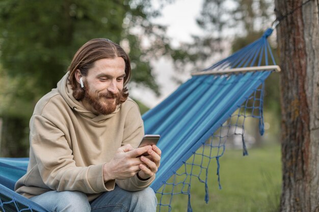 Hombre en hamaca escuchando música en auriculares con teléfono inteligente