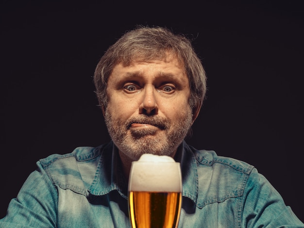 El hombre hechizado en camisa vaquera con vaso de cerveza