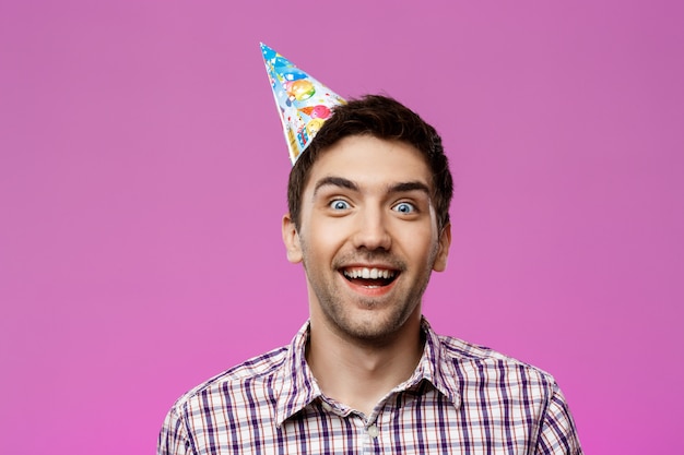 Hombre hermoso joven alegre que sonríe sobre la pared púrpura. Fiesta de cumpleaños.