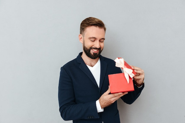 Hombre hermoso joven feliz que mira el regalo rojo aislado