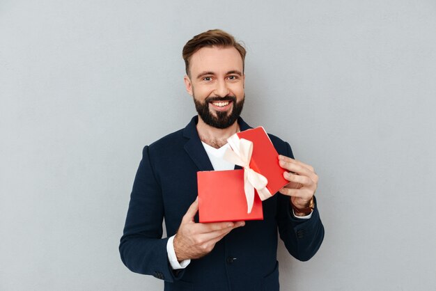 Hombre hermoso joven feliz que mira el regalo rojo aislado