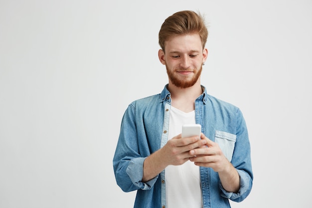 Hombre hermoso joven feliz que sonríe mirando el teléfono que navega el web de la navegación por Internet.