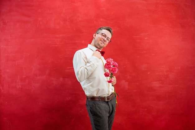 Hombre hermoso joven con flores sobre fondo rojo studio