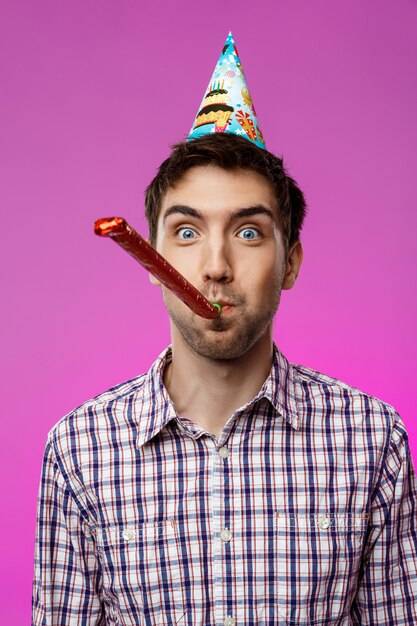 Hombre hermoso joven que celebra la fiesta de cumpleaños sobre la pared púrpura.