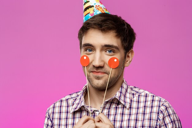 Hombre hermoso joven que celebra la fiesta de cumpleaños sobre la pared púrpura.