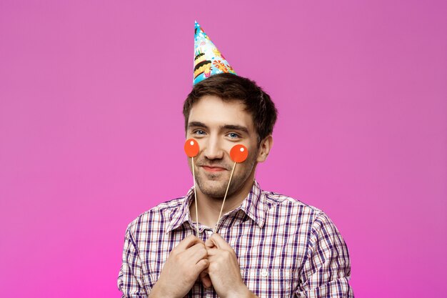 Hombre hermoso joven que celebra la fiesta de cumpleaños sobre la pared púrpura.