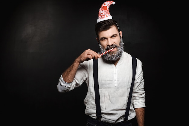 Hombre hermoso joven que come el caramelo de la Navidad sobre negro.