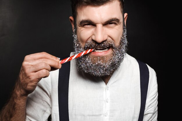 Hombre hermoso joven que come el caramelo de la Navidad sobre negro.