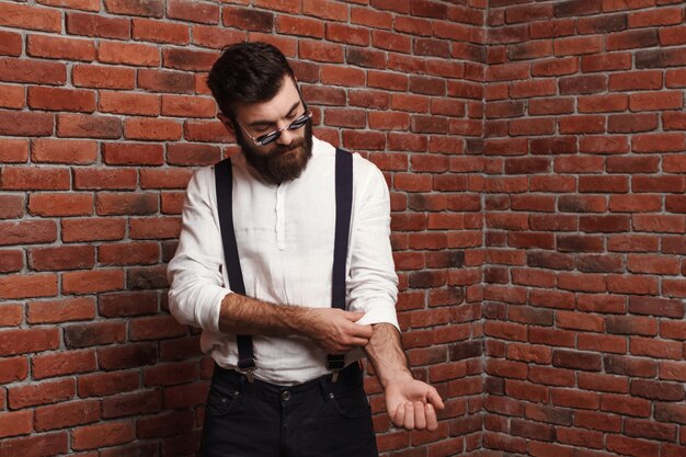 Hombre hermoso joven que corrige la camisa en la pared de ladrillo.